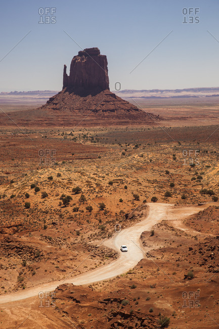 A road winds it's way among a desert landscape with buttes in the background.