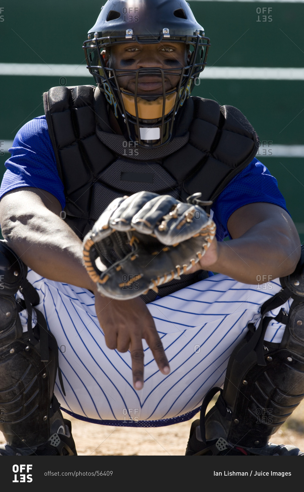 Baseball catcher crouching on pitch, making secret signal with fingers, front view, portrait