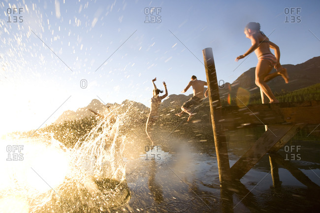 Couple and daughter (8-10) jumping off jetty, low angle view (lens flare)