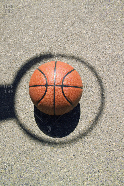 A basketball in the middle of a shadow hoop