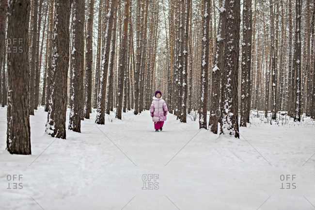 A young girl walking down a snow packed path in the forest