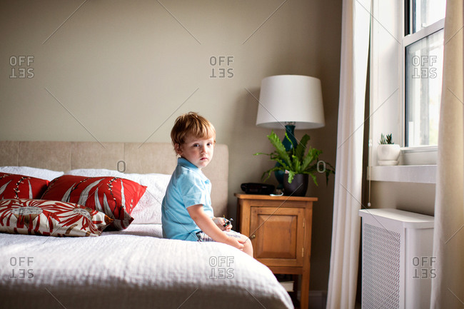 Little boy sitting on his parents bed in bedroom