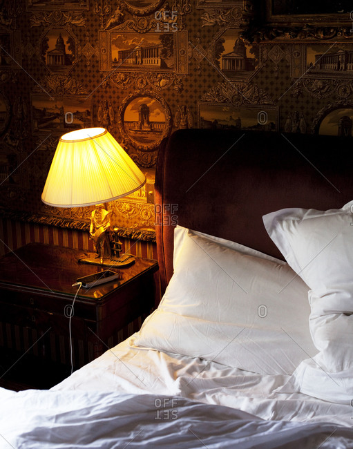 Close up of a bed with bedclothes and an antique lamp