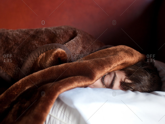 Close up of young boy sleeping with face covered with blanket