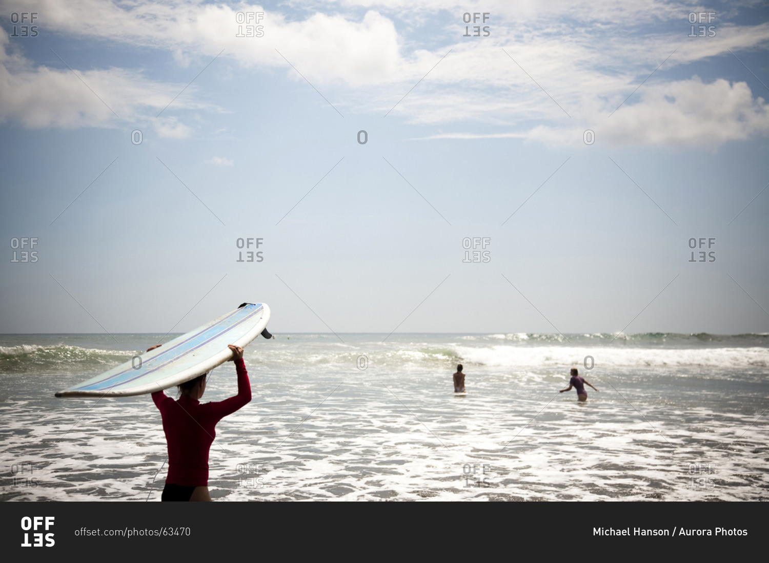 A woman wades out into the ocean with her surfboard resting on her head ...