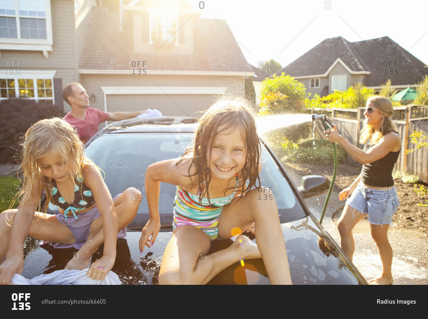 A family washes their car in the driveway of their home on a sunny summer afternoon in Portland, Oregon, USA