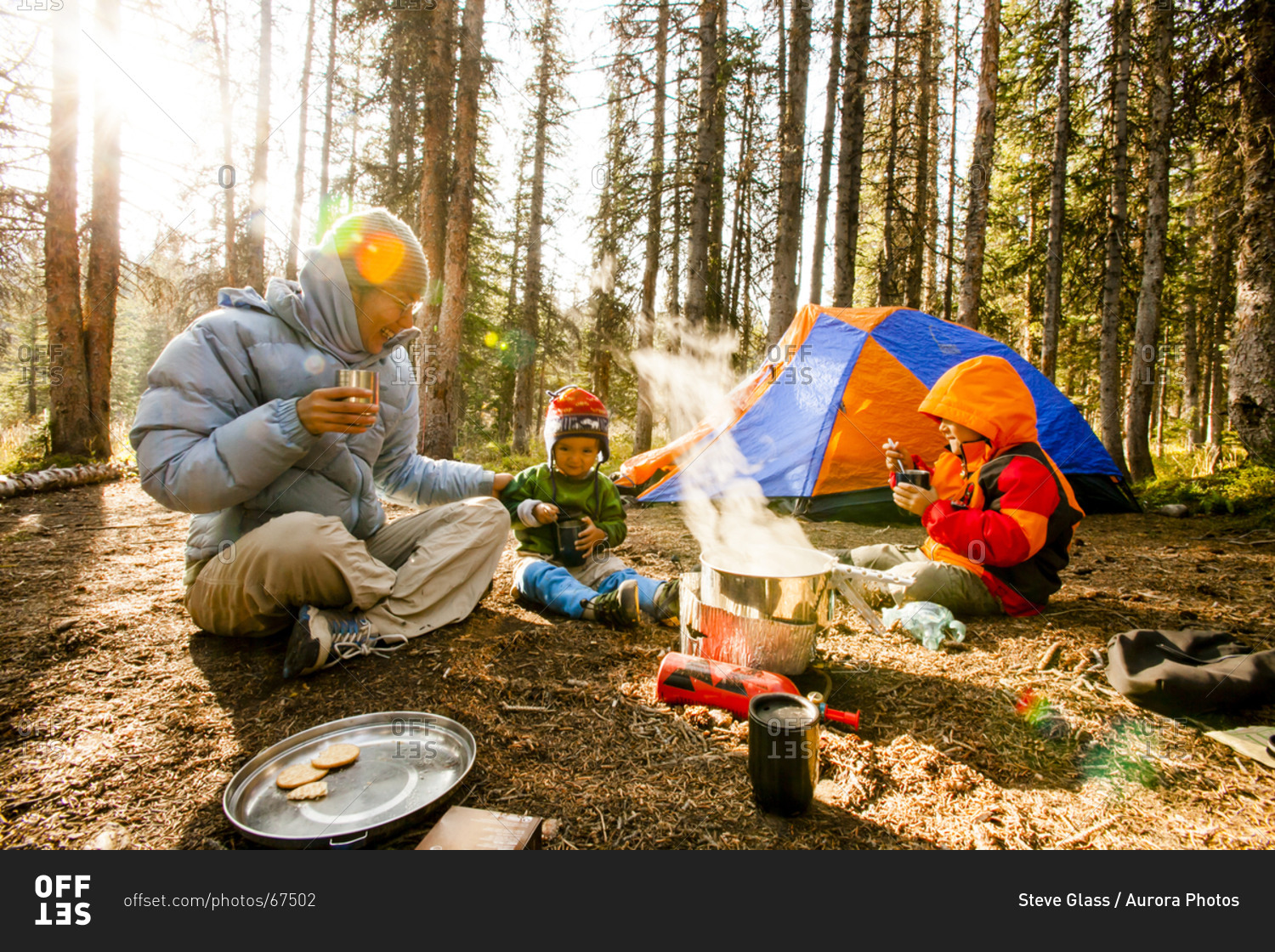 Mother sits with her two boys around the steaming hot stove, in their campsite