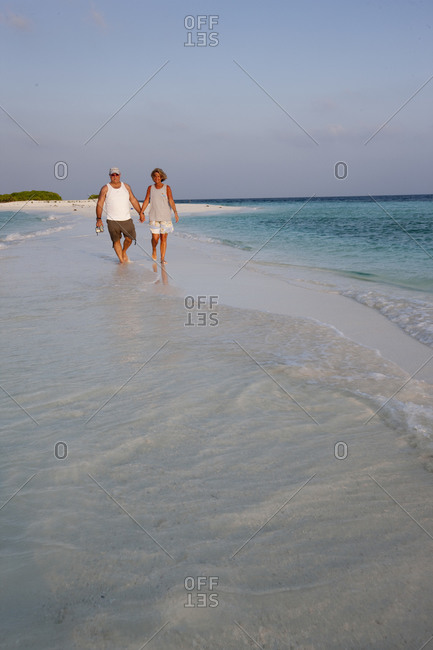 Couple walk on beach on a remote atoll in the Maldives chain, Indian Ocean