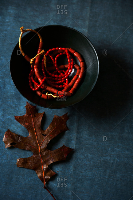 Close-up of red beaded necklace in a bowl with brown autumn leaf