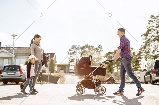 Side view of parents with baby carriage and daughter walking on street