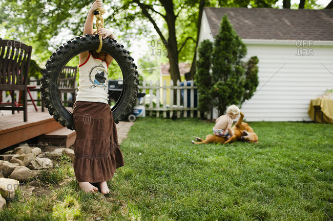 A little girl playing on a tire swing and a little boy wrestling with dog