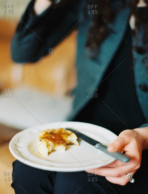 A person holding a plate, holding a half eaten scone with jam