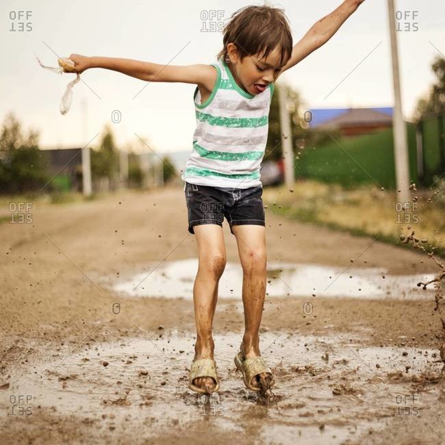 Boy playing in muddy puddle outdoors