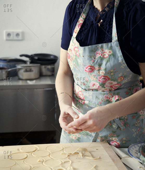 Mid section view of woman in floral pattern apron cutting dough