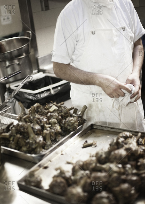 Mid section view of man standing in kitchen with piles of roasted artichokes