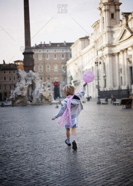 Young girl running with pink balloon toward the fountain in Piazza Navona, Rome
