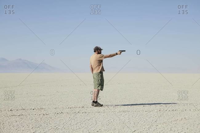 Man aiming hand gun, standing in vast, barren desert