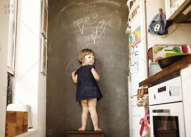 Girl standing on a step ladder in front of a chalkboard wall