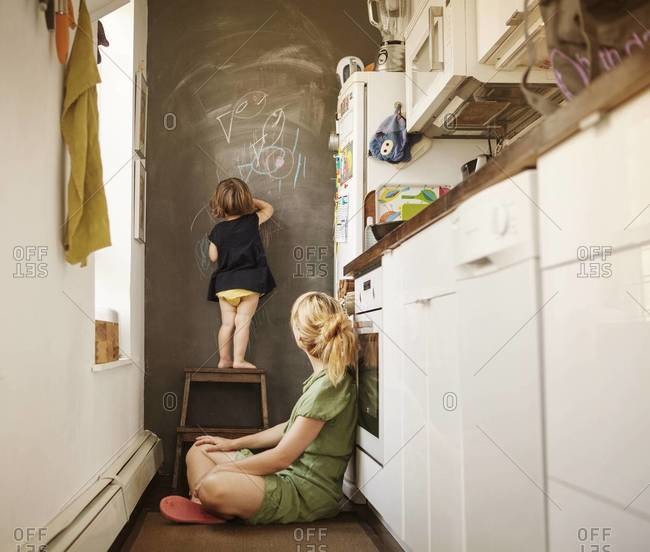 Woman watching a toddler drawing on the chalkboard wall