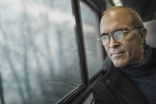 A mature man sitting in a window seat on a train journey, looking out into the distance.