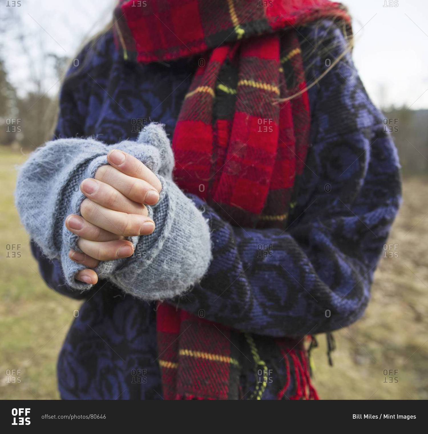 A woman in a tartan scarf and knitted woolen mitts, keeping her hands warm in cold weather.