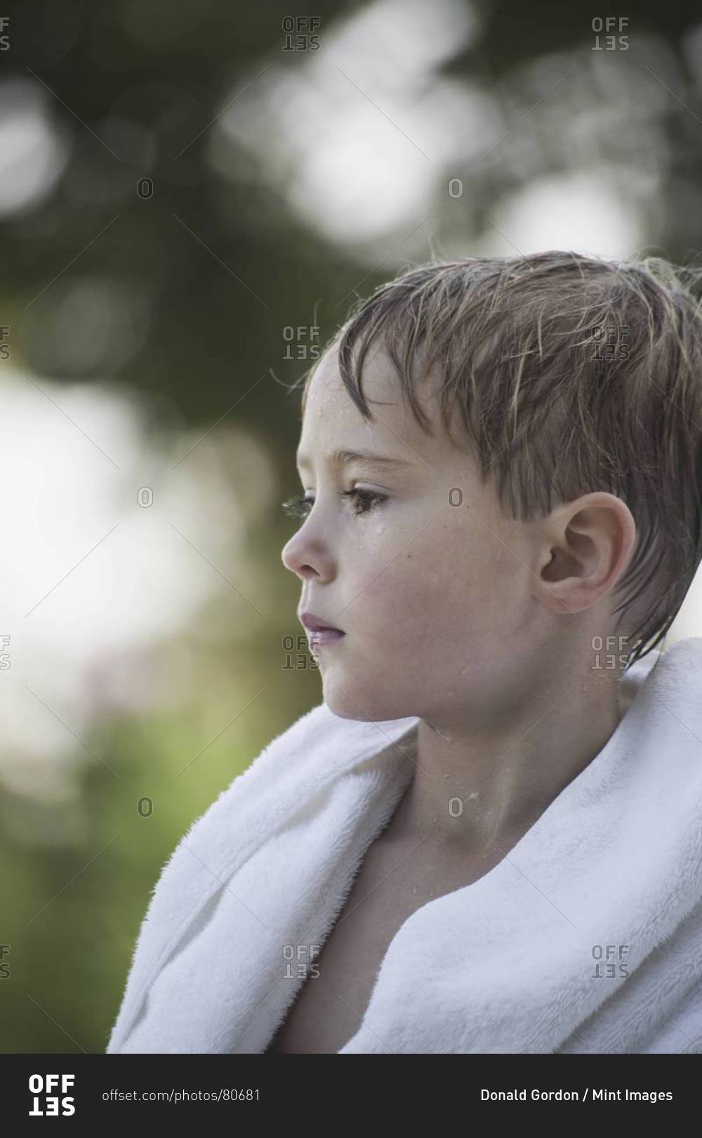 A young boy with wet hair, wrapped in a towel after swimming. stock