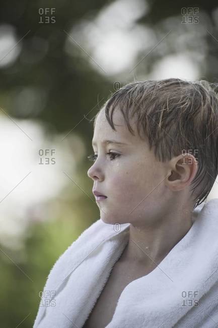 A young boy with wet hair, wrapped in a towel after swimming.