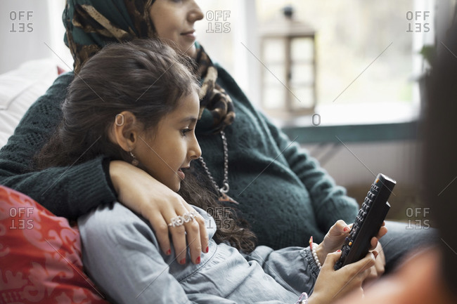 Daughter using remote control while sitting with mother at home