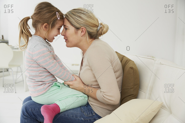 Mother cuddling with daughter sitting on sofa