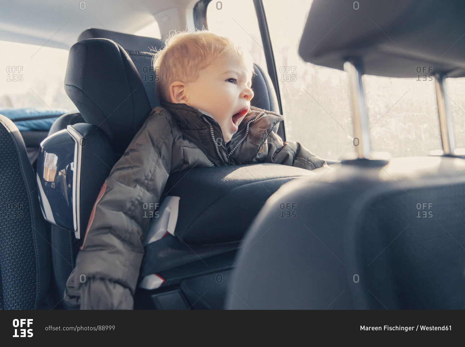 Little boy sitting in back-seat car seat, yawning