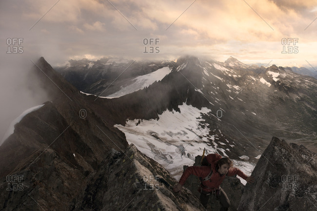 A mountaineer climbs toward a summit overlooking a foggy valley with glaciers.