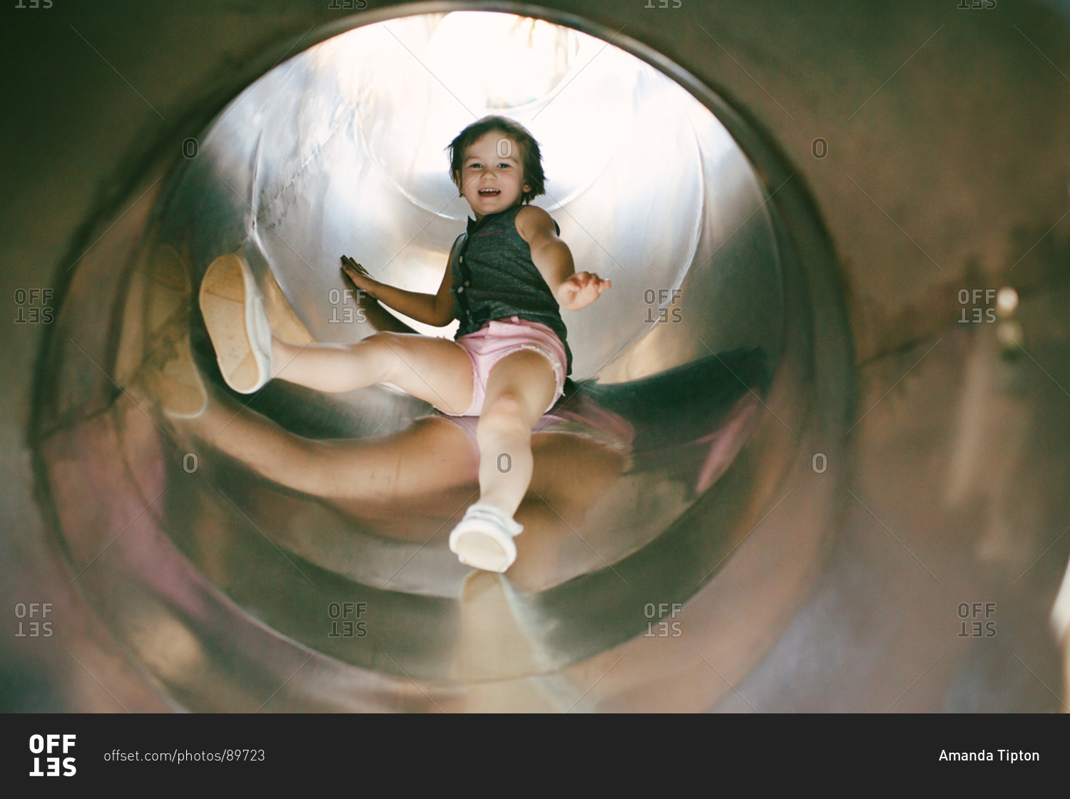 Little girl sliding down a covered slide stock photo - OFFSET