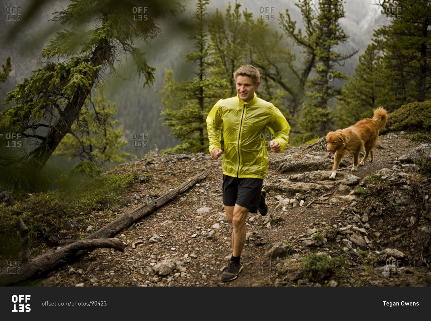 Athletic young man runs on a mountain trail with a happy dog