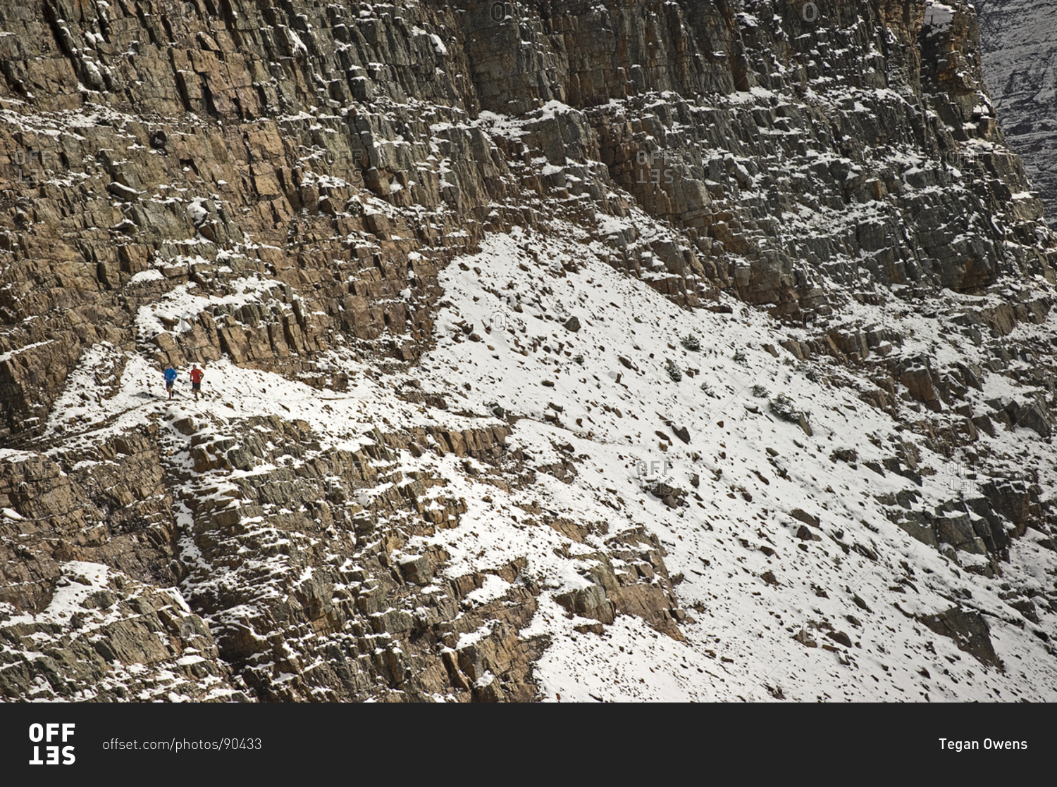 Two men run on a rocky, snowy mountain trail