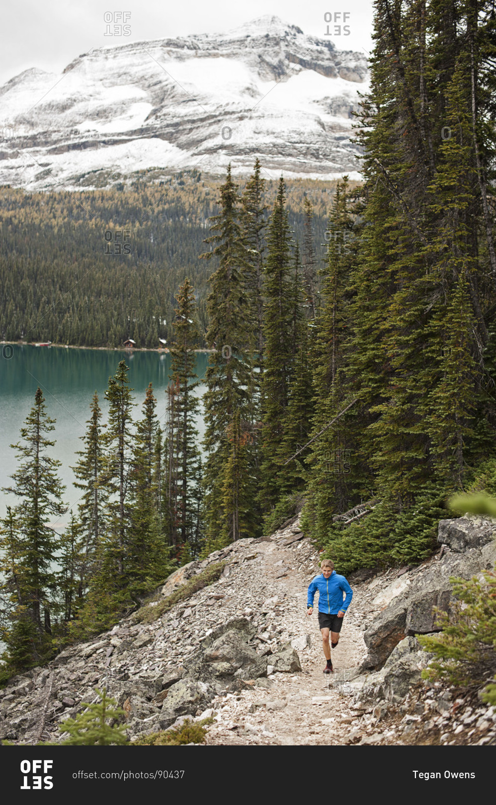 Athletic young man runs on a mountain trail beside a lake