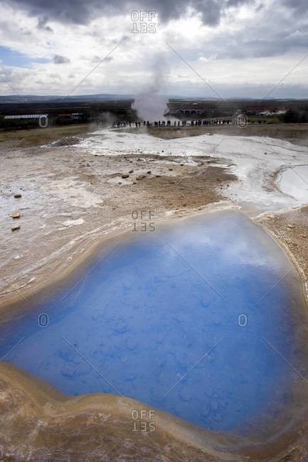 Blue water in geothermal pool with stream from Strokkur Geysir visible in the distance, Geysir, near Reykjavik, Iceland, Polar Regions