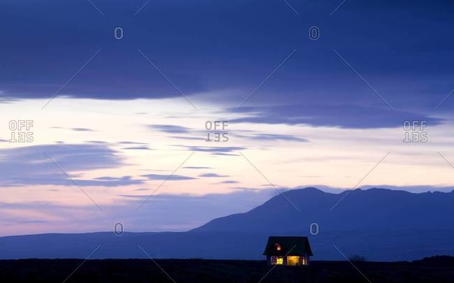 Twilight view towards mountains with small house illuminated by interior lights, near Hella, South West Iceland, Iceland, Polar Regions