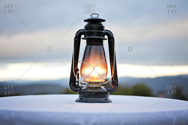 An antique gas lantern sits on a tabletop in the fading twilight.