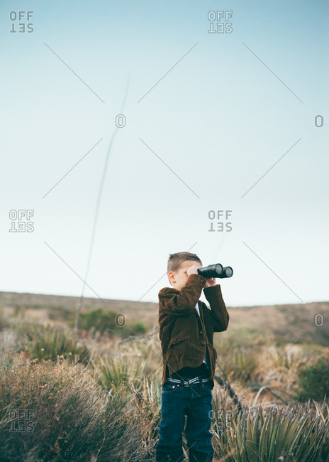 Young boy looking through binoculars in the wilderness