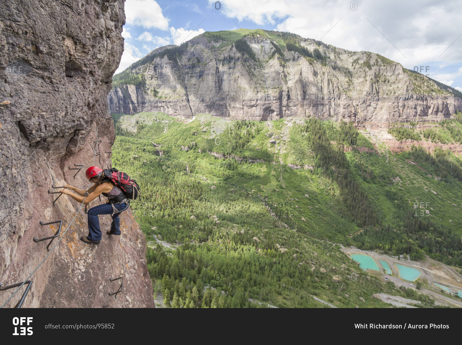 A woman traversing a rock wall using metal rungs in the moutains. stock