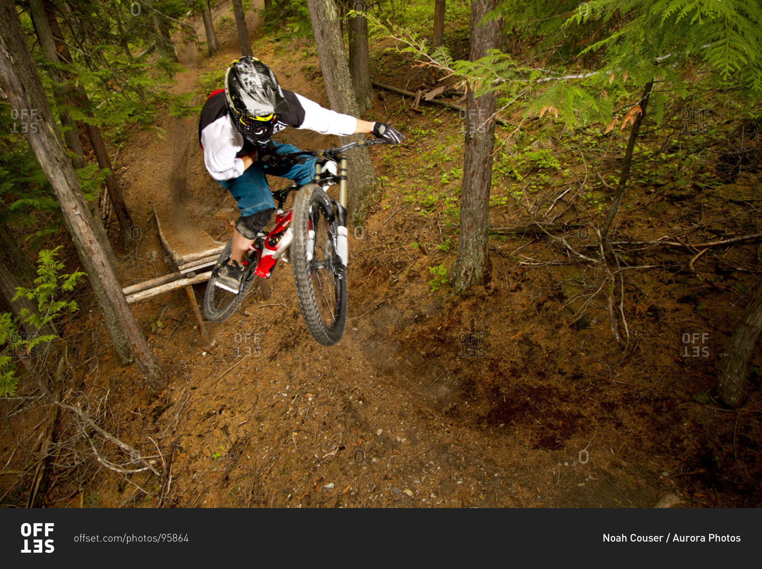 A downhill mountain biker jumps his bike through the trees.