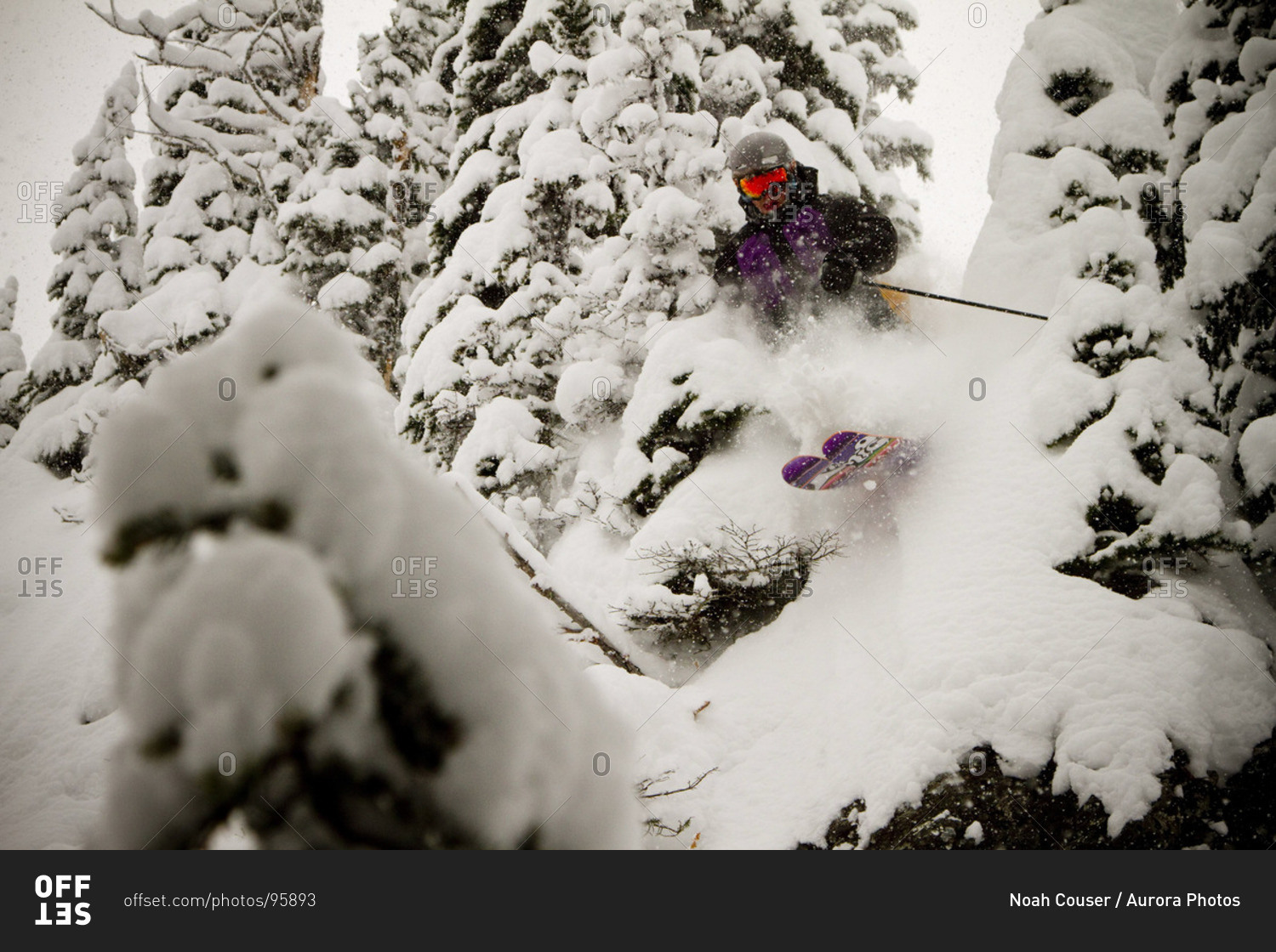 A skier punches through some powder and some trees on a cloudy day.