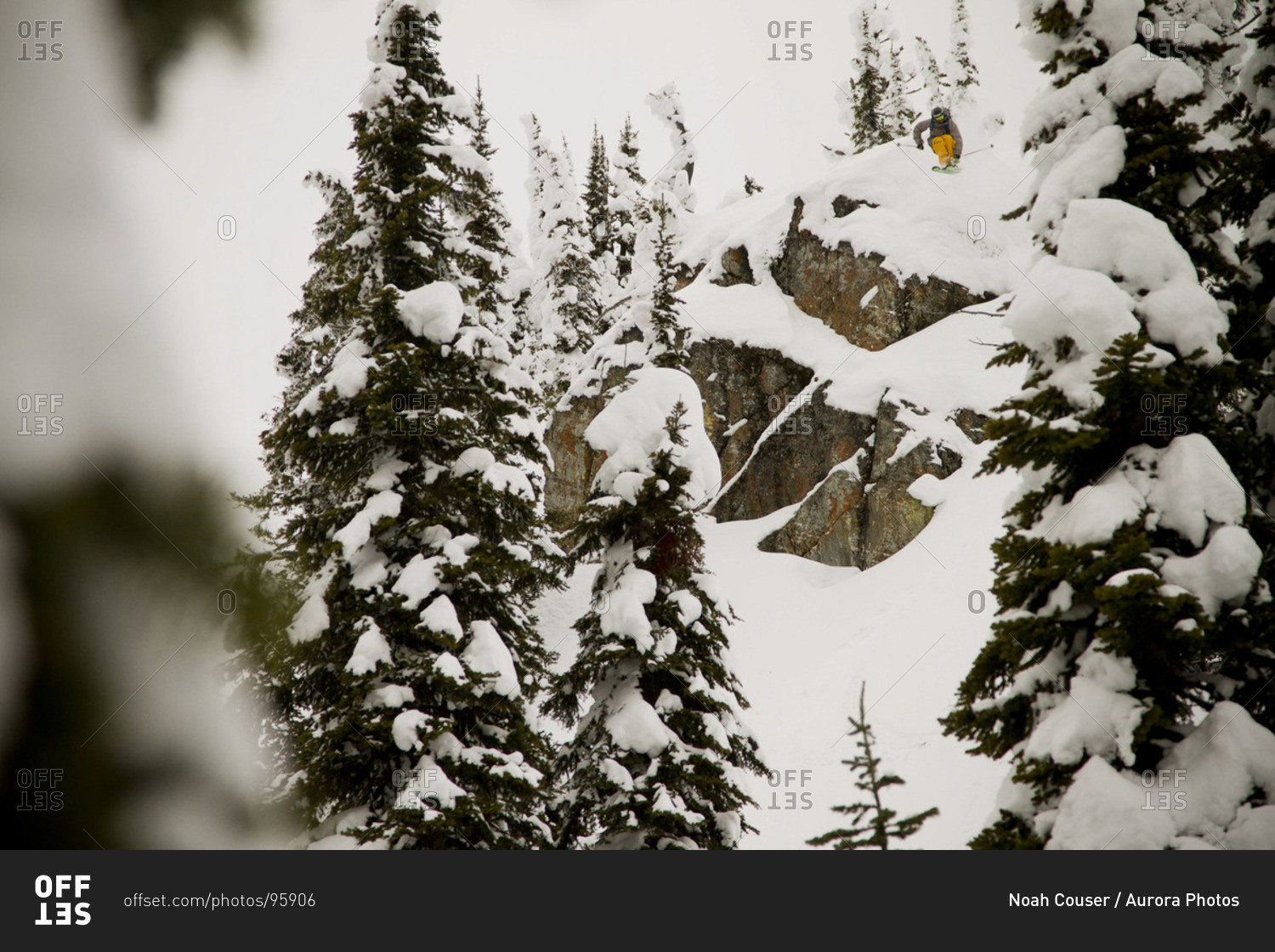 A backcountry skier drops a large cliff on a cloudy day in mid-winter.