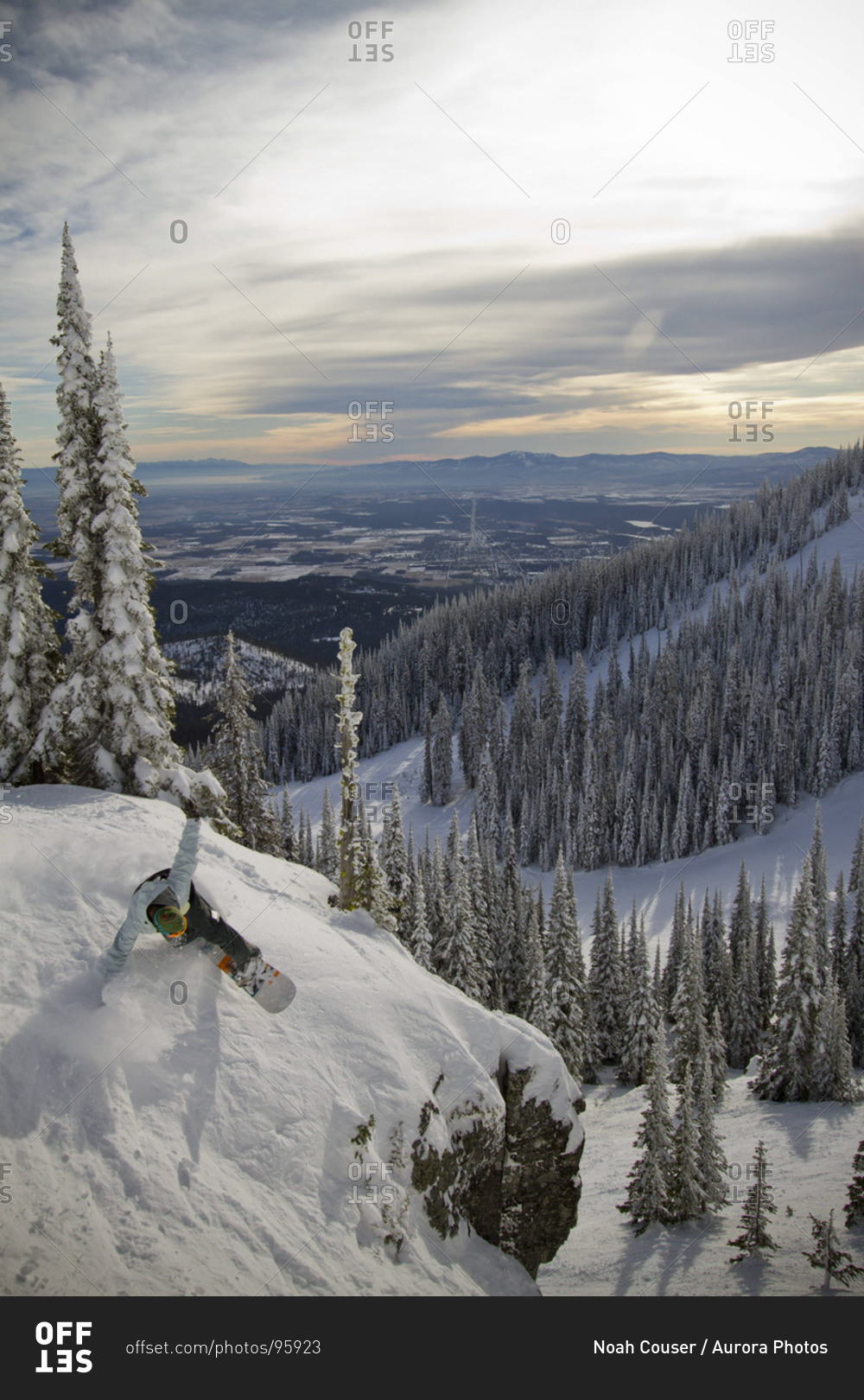 A snowboarder carves a turn atop a cliff on a cloudy winter day.