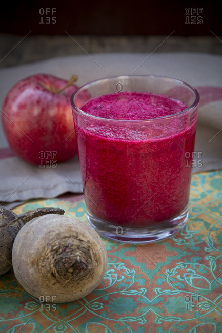 Glass of apple beetroot smoothie, apple and two beetroots on table