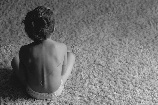 Overhead view of shirtless boy sitting on carpet