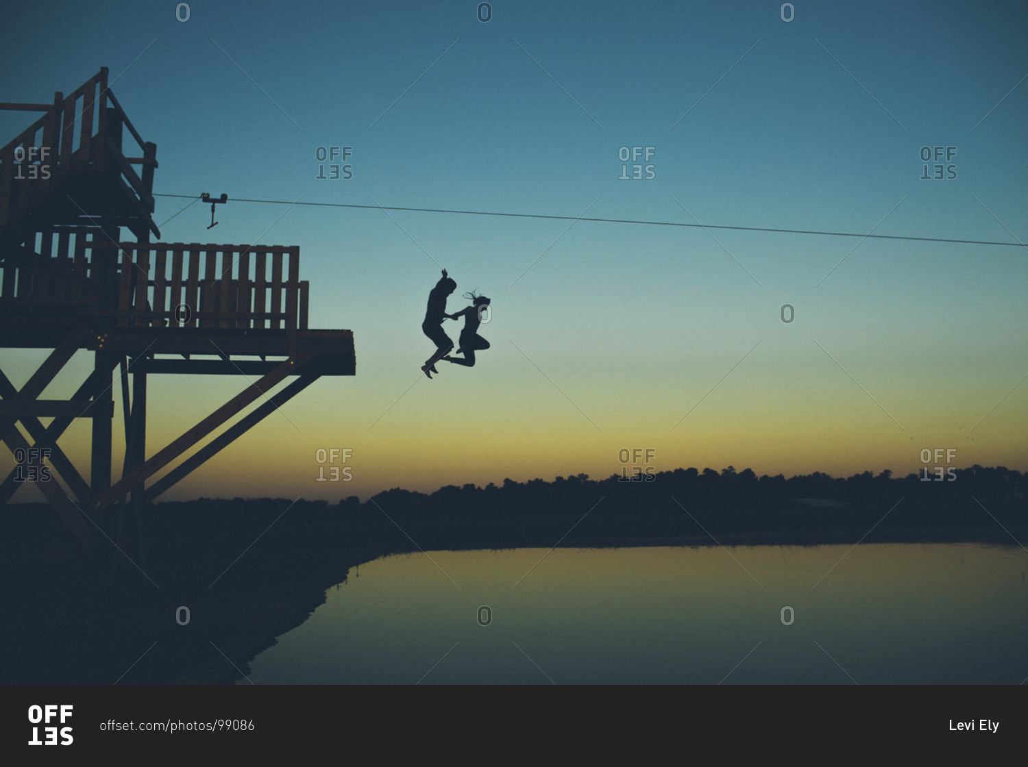 Silhouette of couple jumping into lake water in twilight