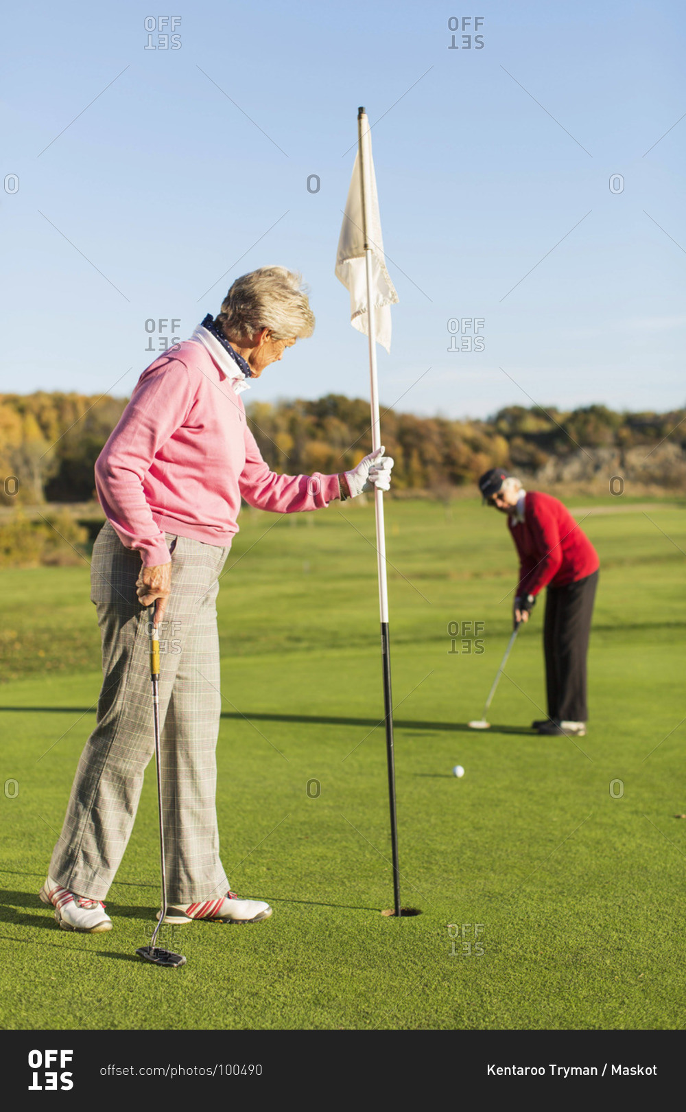 Senior woman putting while friend holding flag on golf course