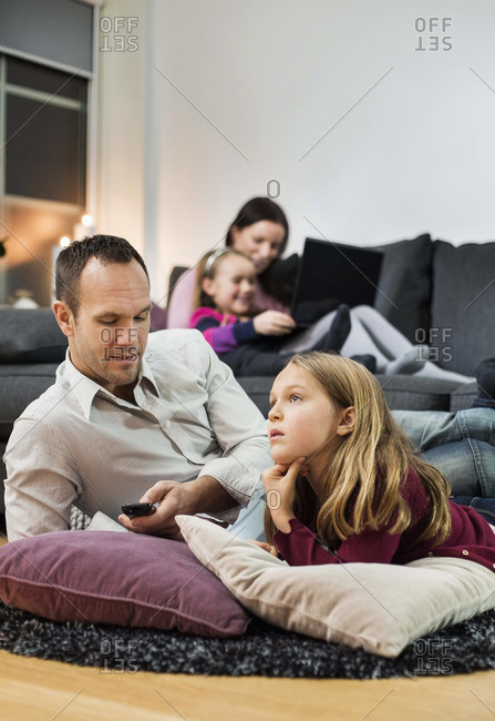 Father and daughter watching TV on floor with family in background