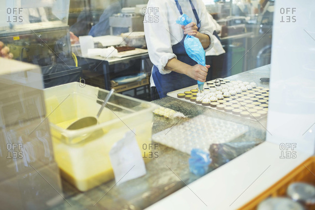 Midsection Of Female Worker Icing Sweet Food At Display Cabinet In